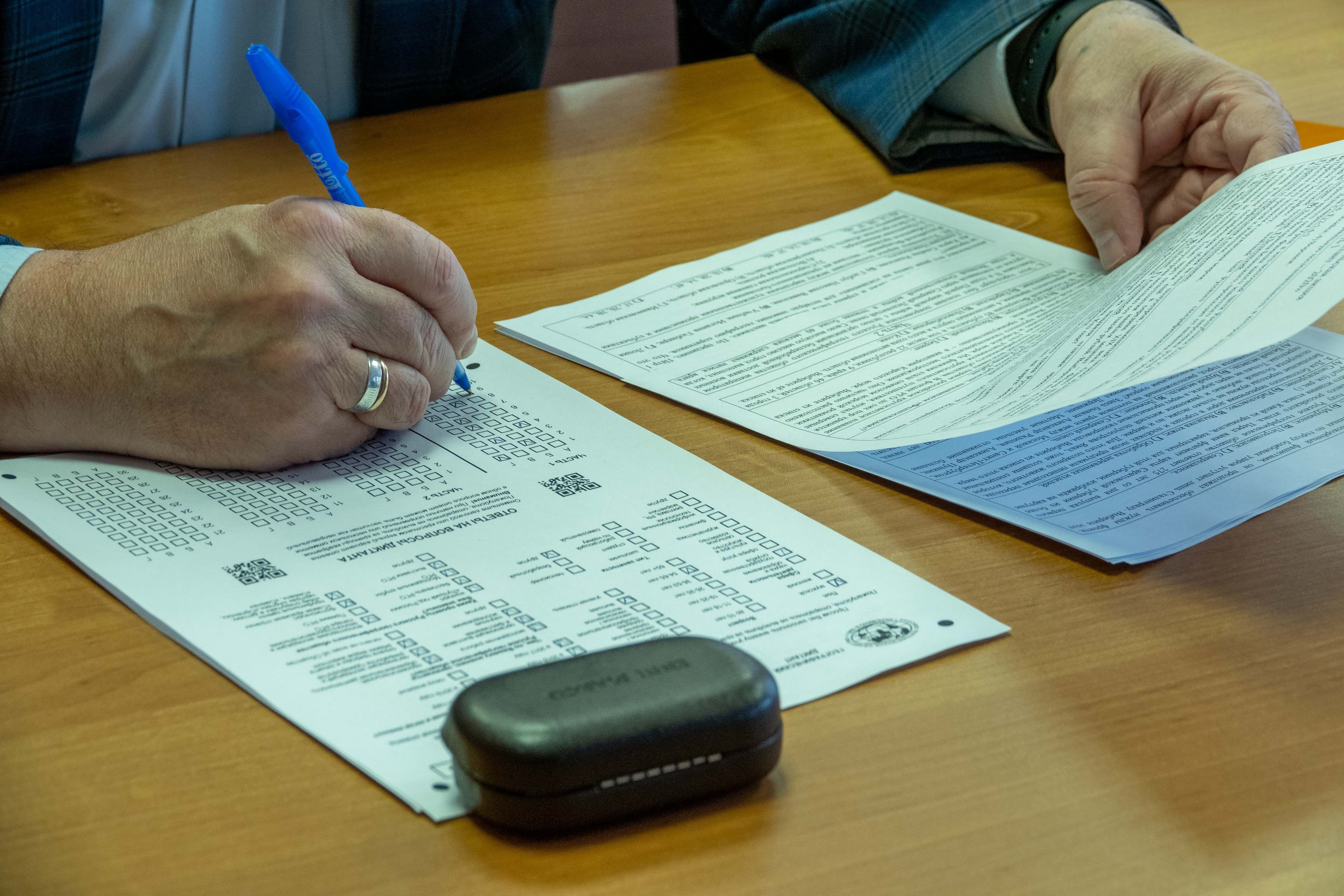 Hands filling a paper form across a wooden desk